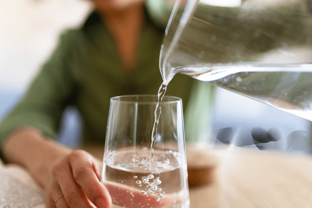 Close-up image of a woman pouring water from a jug into a glass, symbolizing the importance of staying hydrated.