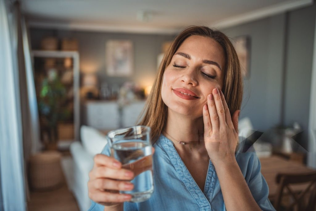 Young woman smiling while holding a glass of clean, fresh drinking water, promoting a healthy lifestyle and hydration.